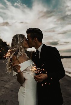 a newly married couple kissing on the beach with sparklers in front of their faces