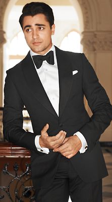 a man in a tuxedo is posing for a photo with his hands on his hips