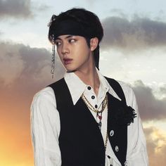 a young man wearing a black vest and white shirt standing in front of a cloudy sky