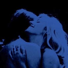 two people are kissing in the dark with blue lighting on them and one person has his arm around the woman's shoulder