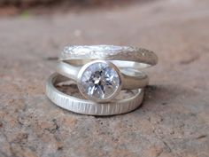 two silver rings with a diamond in them sitting on top of a stone surface next to each other