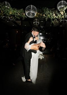 a bride and groom dance together at their wedding reception in the dark with chandeliers hanging from the ceiling