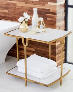 a gold and white table with towels on it next to a bathtub, toiletries and vase