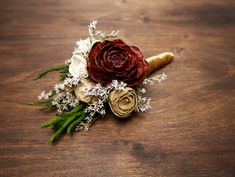 a boutonniere with white and red flowers on a wooden table next to other items