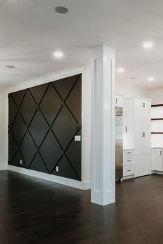 an empty room with white cabinets and wood flooring in the center is a black diamond pattern on the wall