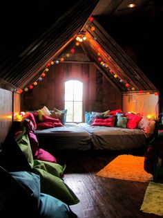 an attic bedroom with two beds and pillows on the floor in front of a window