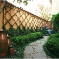 a stone path between two large vases in front of a wooden fence with ivy growing on it