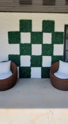 two brown wicker chairs sitting next to each other on a cement patio with grass covering the wall behind them