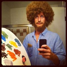 a man with an afro is holding a cell phone and looking at his selfie