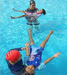 three people are in the water with their hands up and one person is wearing a red hat