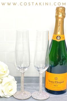 two champagne glasses and a bottle of wine on a table with flowers in the background