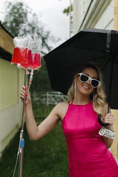 a woman in a pink dress holding an umbrella and two glasses with liquid inside it