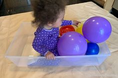 a toddler playing with balloons in a plastic container