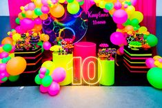 the table is set up with neon colored balloons and streamers for an 10th birthday party