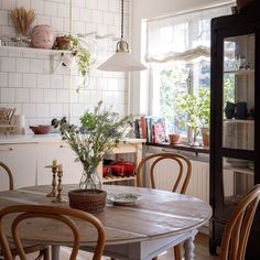 a dining room table and chairs in front of a window with potted plants on it