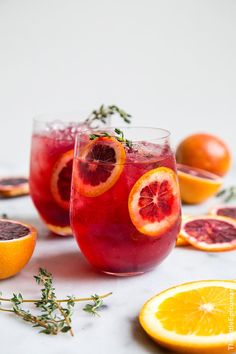 two glasses filled with blood orange punch and garnished with herbs