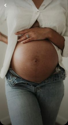 a pregnant woman wearing jeans and a white shirt is holding her belly in the air