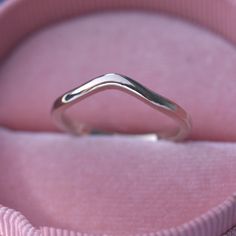 a silver ring sitting on top of a pink velvet box with the lid open to show it's wavy shape