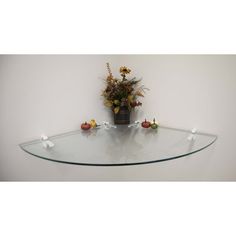 a glass table with flowers and candles on it in front of a white wall background