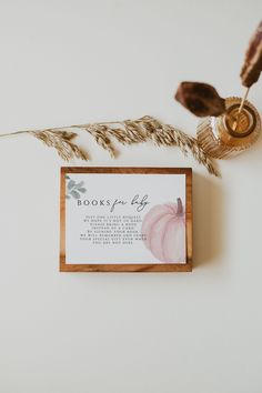 a wooden frame with a card on top of it next to a plant and a feather