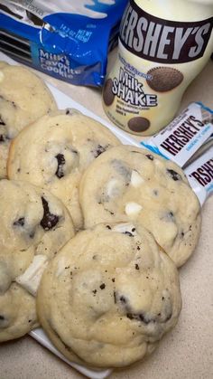 chocolate chip cookies and milk are on a plate next to some ice cream, two spoons and a bag of hershey's