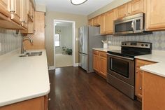 an empty kitchen with stainless steel appliances and wood cabinets in the background, along with white counter tops