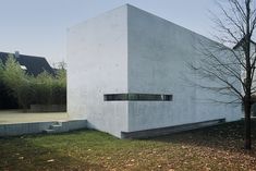 a concrete building sitting on top of a grass covered field next to a tree with no leaves