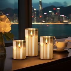 three lit candles sitting on top of a table next to a vase filled with flowers