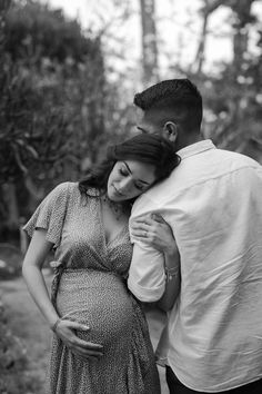 a pregnant couple cuddles in the woods for their black and white photo session