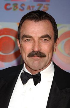 a man in a tuxedo and bow tie poses for the camera at an event