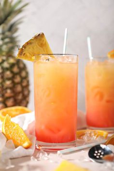 two glasses filled with orange juice and garnished with pineapple on the side