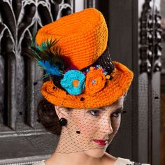 a woman wearing an orange hat with blue flowers and feathers on it's brim