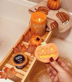 a person holding a pumpkin shaped cookie in front of a bathtub filled with fall leaves