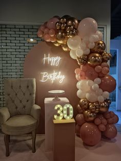 a balloon arch that says happy birthday with balloons around it and a chair in front