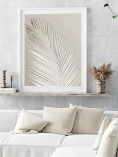 a living room with a white couch and a framed palm leaf art print on the wall