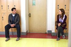 two people sitting on chairs in front of lockers, one is talking to the other