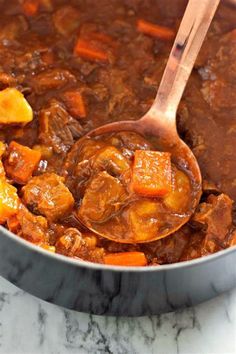 a ladle full of stew with carrots and potatoes in it on a marble counter top