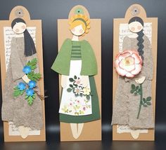 three paper dolls with flowers on them sitting in front of some brown cardboard tags that have been cut out to look like women