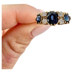 a woman's hand holding an antique ring with blue stones and diamonds on it