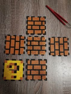 four pieces of perler bead are laid out on a wooden table next to a pair of knitting needles