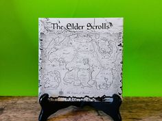 the elder scrolls book stand on a wooden table against a green background with an old map