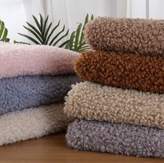 a pile of towels sitting on top of a wooden table next to a plant and window