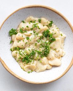 a white bowl filled with ravioli and parsley sprinkled on top of it