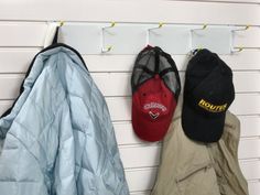 three hats hanging on the wall next to coats and jacket hooks, one with a baseball cap