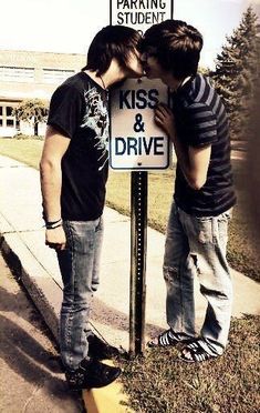 two young men standing next to a kiss and drive sign on the side of a road