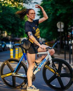 a woman riding a bike down the street with her arm in the air and one hand up