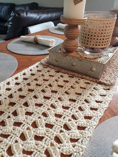 a crocheted table runner on top of a wooden table next to a candle