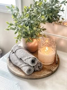 a candle and some towels sitting on a tray next to a potted plant in front of a mirror