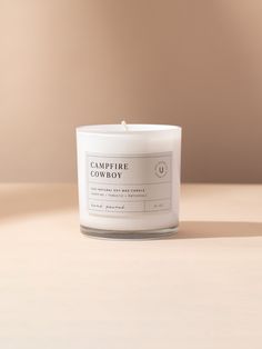 a white candle sitting on top of a table next to a brown wall with the words campfire cowboy written on it