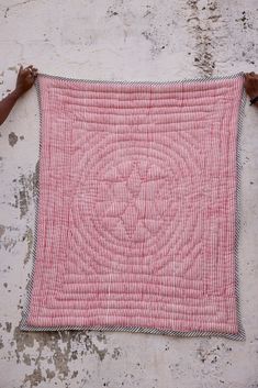 a red and white quilt hanging on the side of a building with two hands holding it